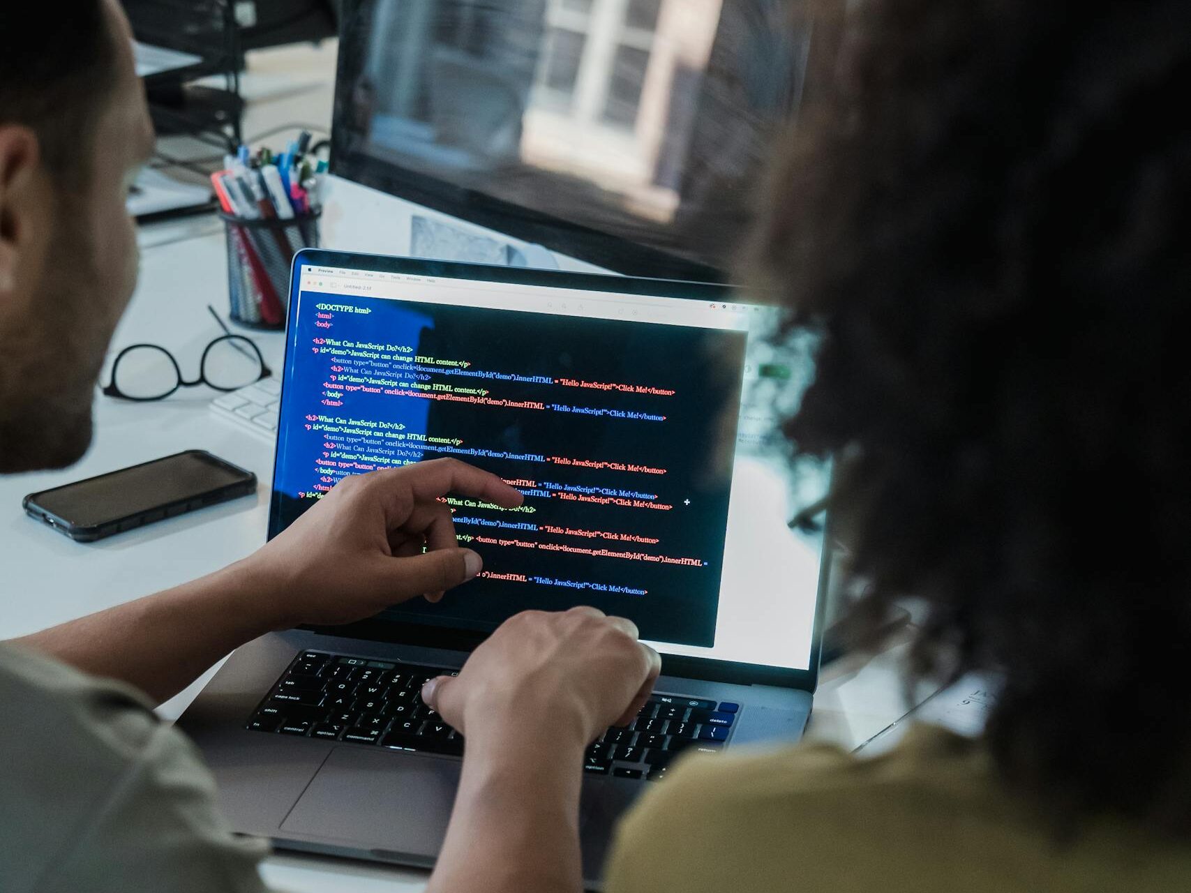 Two adults collaborating on programming tasks using a laptop in an office setting.